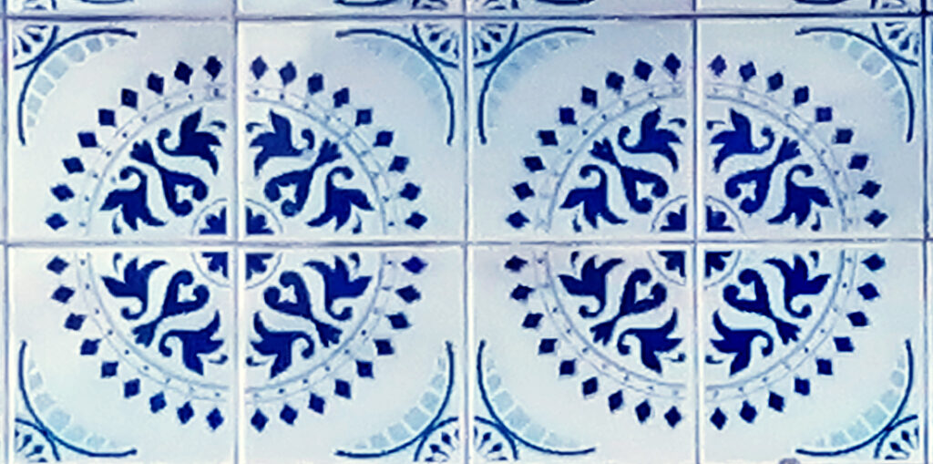 A imagem mostra um padrão de azulejos azuis e brancos com desenhos circulares que ocupam quatro azulejos cada, apresentando motivos florais estilizados e pequenos diamantes azuis, típico da azulejaria tradicional.
